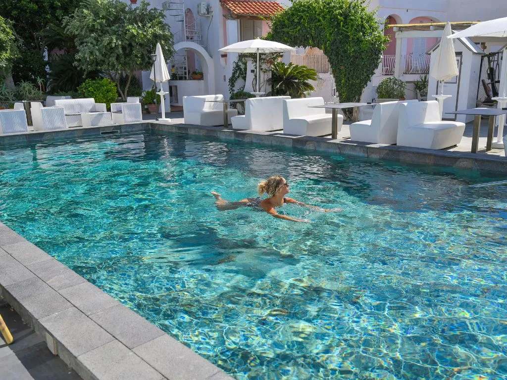 Donna nuota nella piscina esterna con acqua cristallina e divanetti bianchi