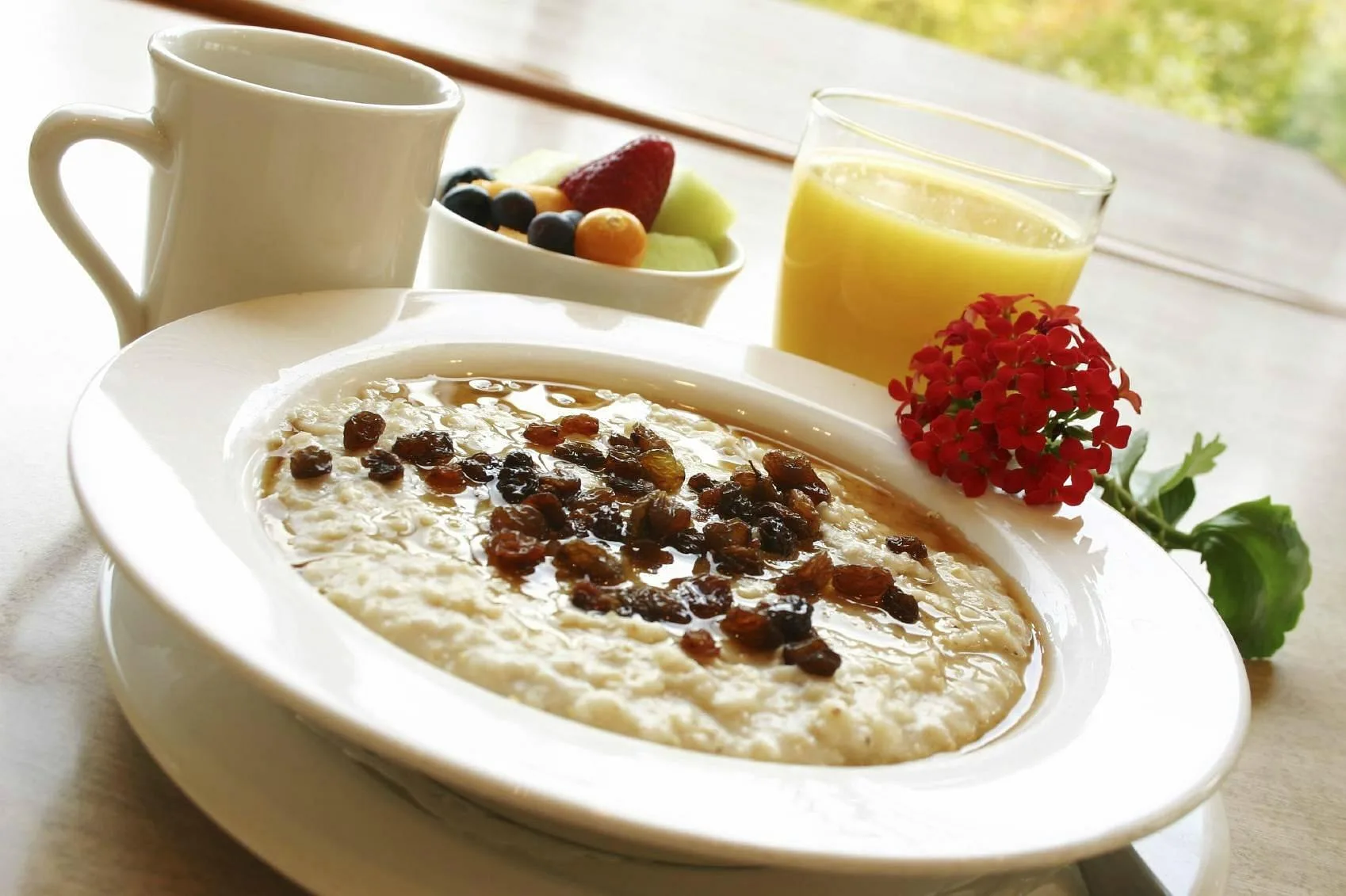 Colazione con porridge, uvetta, frutta fresca e succo d'arancia