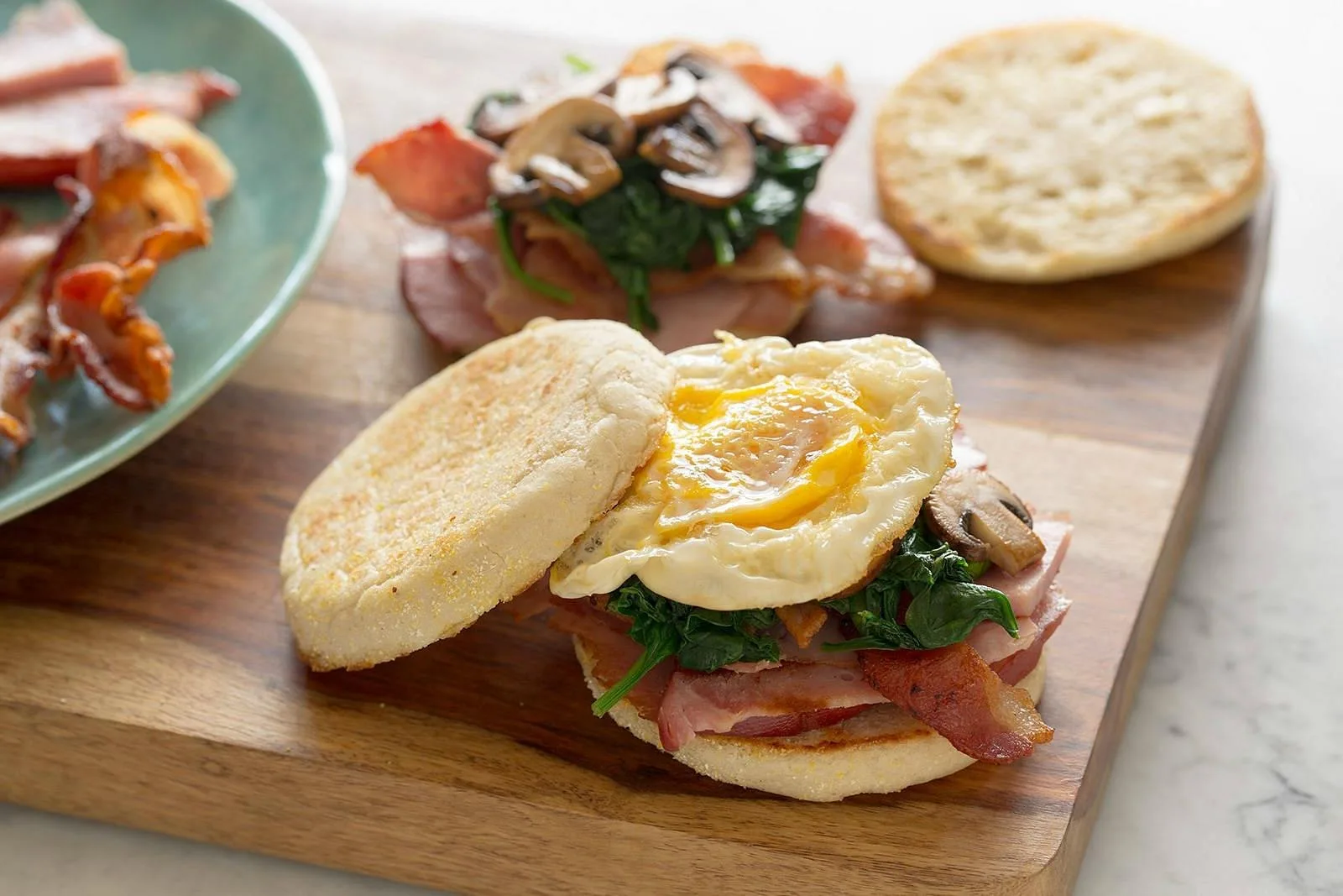 Panino con uovo, pancetta, funghi e spinaci su tagliere di legno