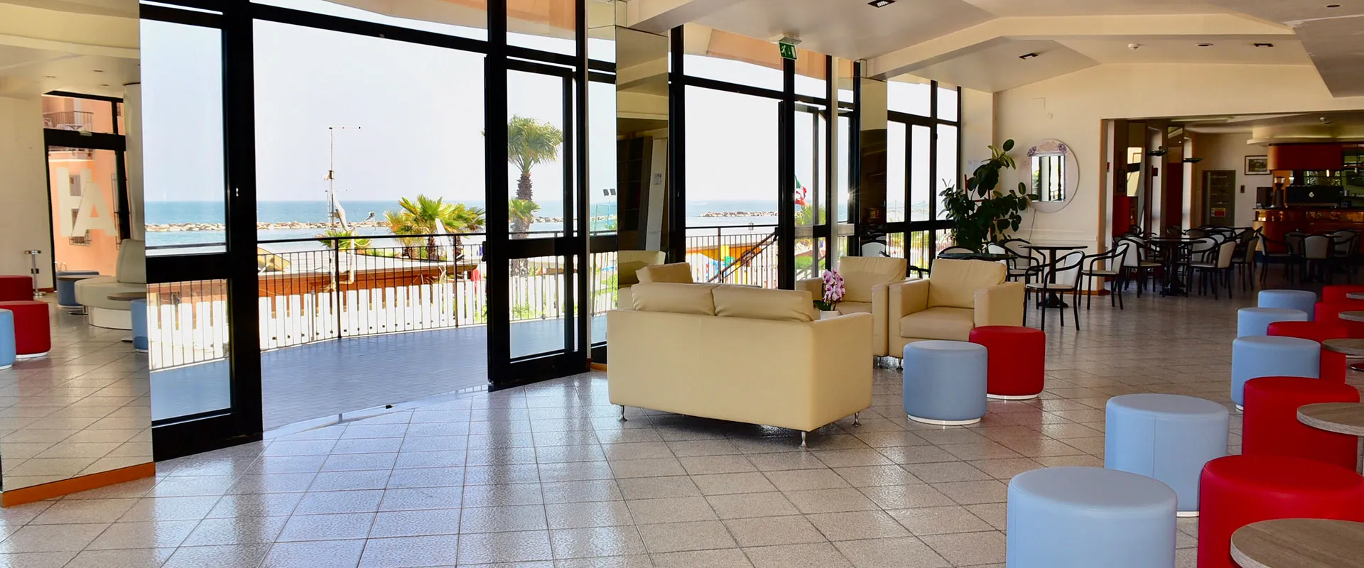 Hall dell'hotel con divani, pouf colorati e ampie vetrate affacciate sul mare
