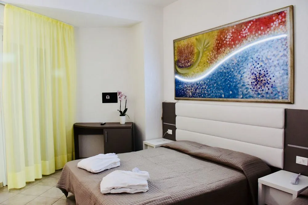 Camera matrimoniale con quadro colorato, tende gialle e asciugamani sul letto