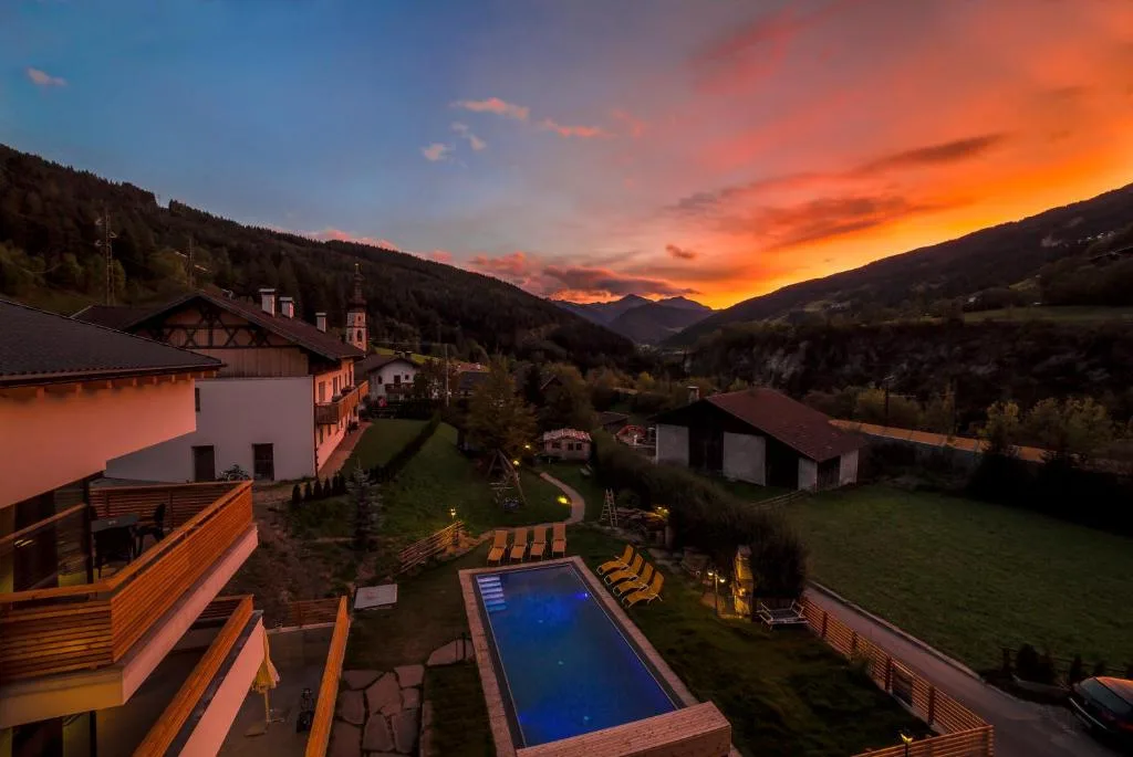 Vista al tramonto sulla valle con piscina esterna, giardino illuminato e cielo arancione