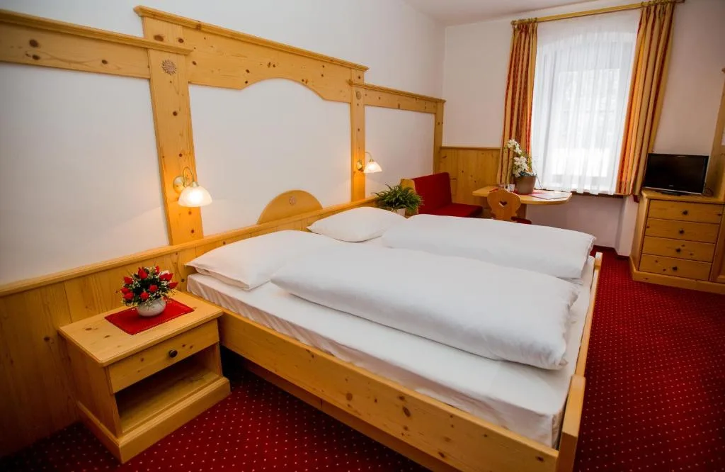 Camera con letto matrimoniale in legno di pino, moquette rossa, TV e poltrona rossa