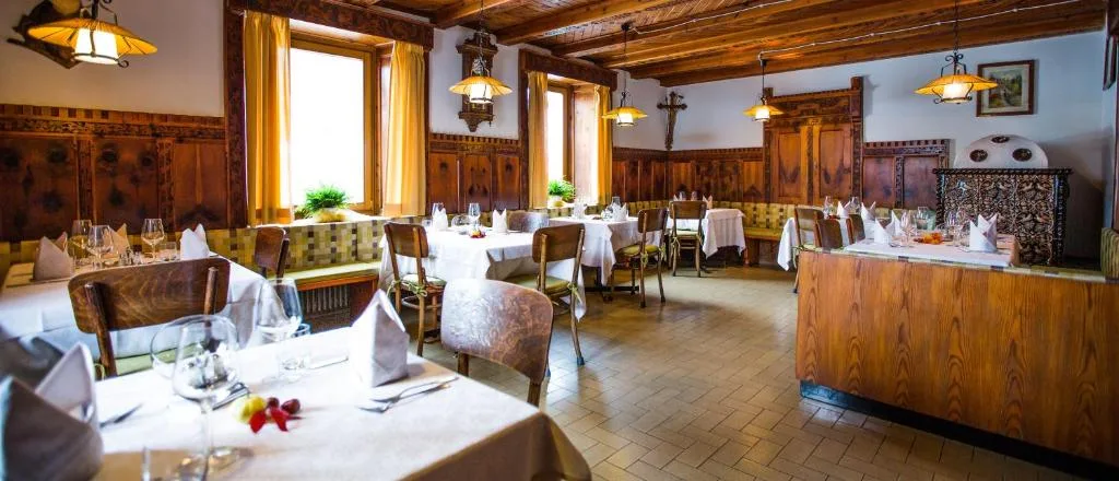 Elegante sala ristorante con boiserie in legno intagliato, stufa in maiolica e tavoli apparecchiati