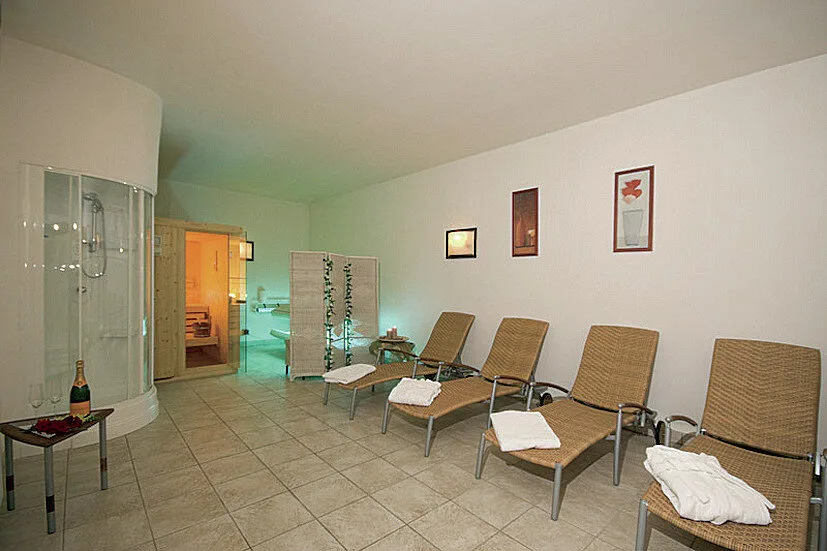 Area relax della spa con lettini in vimini, sauna e cabina doccia, illuminazione soffusa