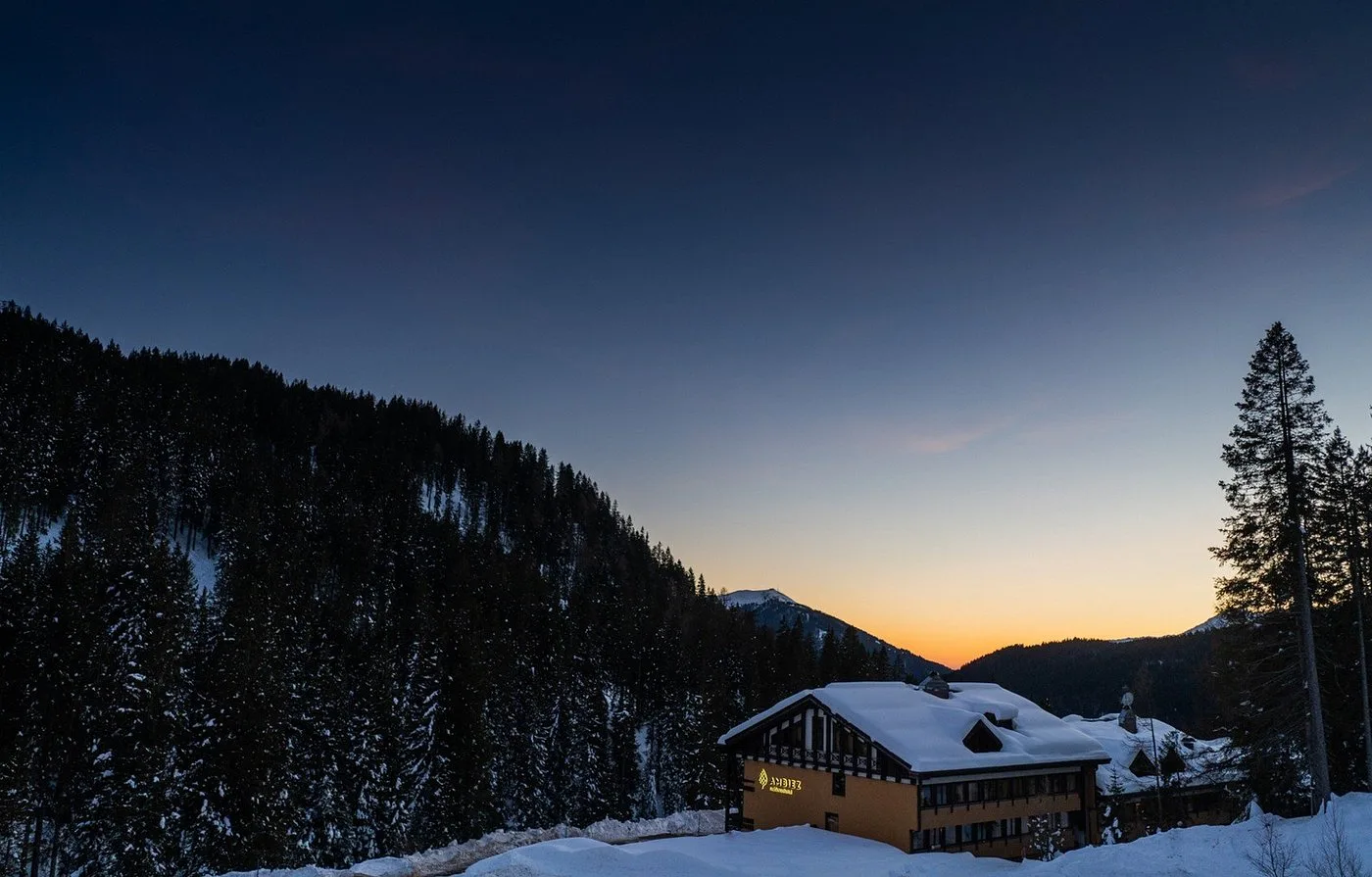 Hotel Ambiez al crepuscolo immerso nel bosco innevato con cielo arancione