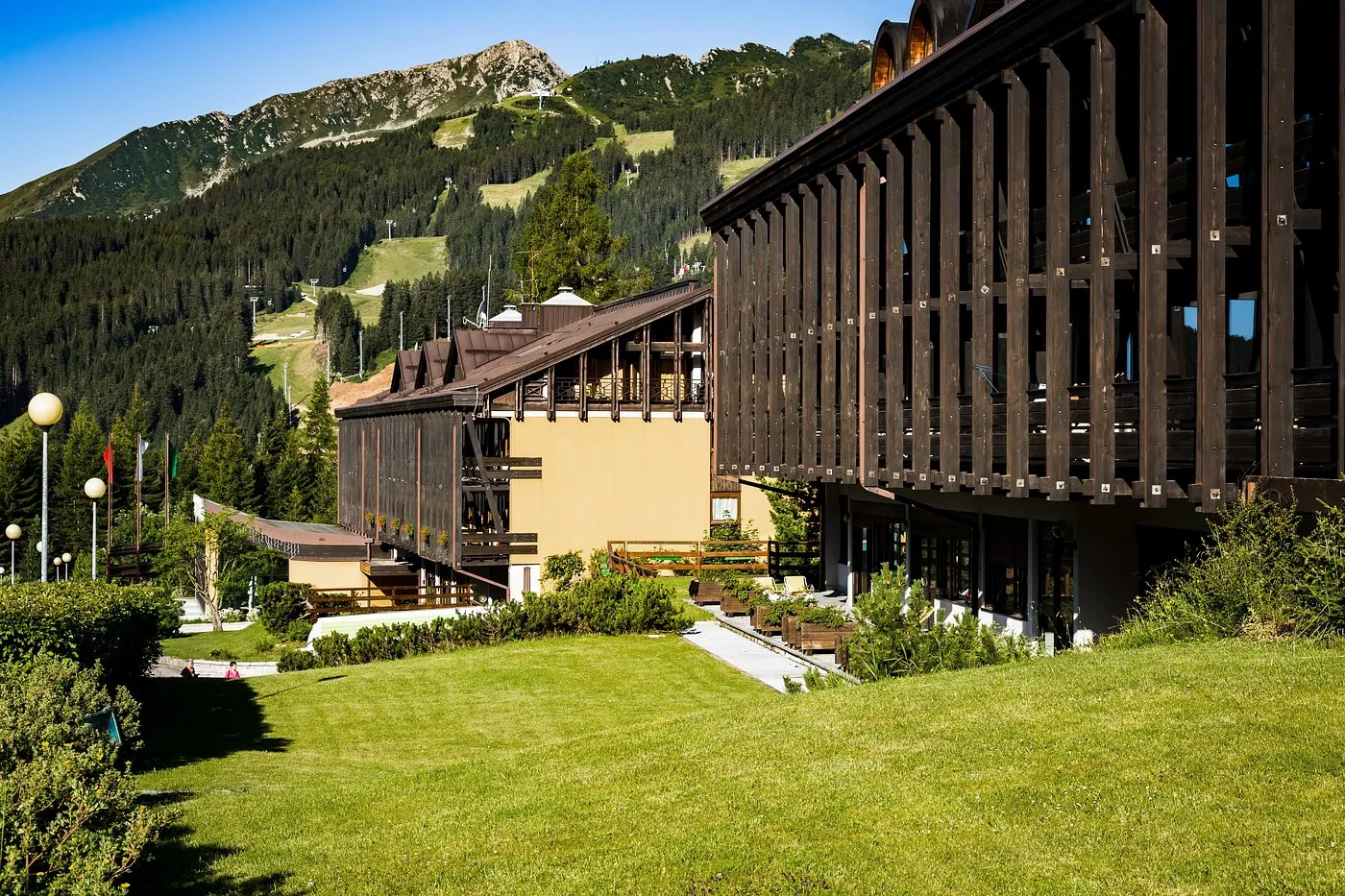 Veduta estiva della facciata in legno dell'hotel con prato verde e montagne