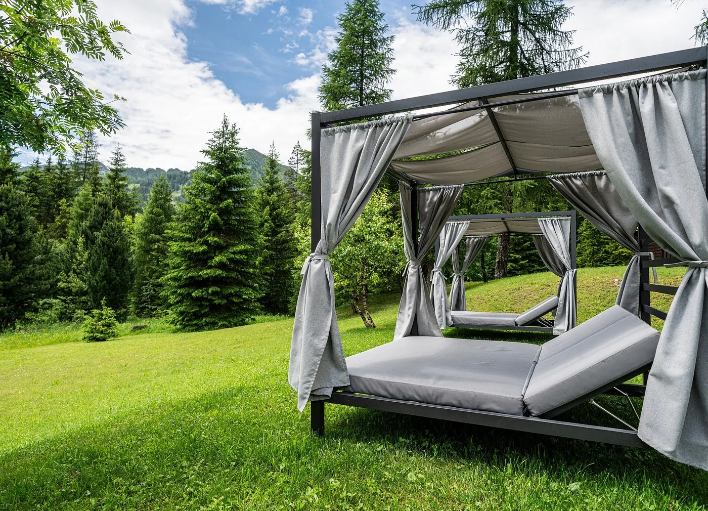 Letto baldacchino da esterno con tende grigie nel giardino verde dell'hotel