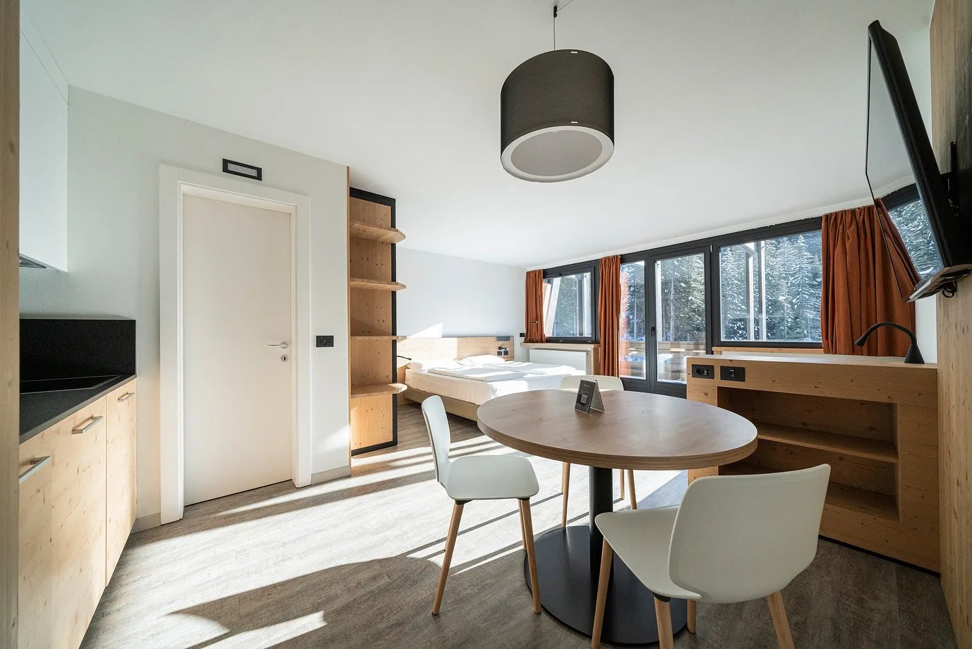 Monolocale moderno con angolo cottura, letto e tavolo rotondo con vista sul bosco
