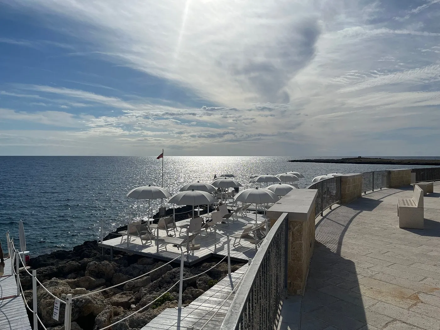 Terrazza sul mare con ombrelloni bianchi e solarium sulle rocce