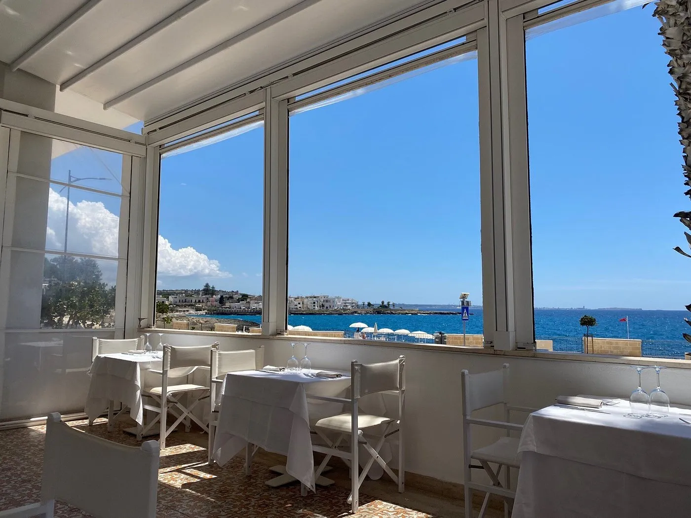Sala ristorante con tavoli bianchi e ampie vetrate affacciate sul mare