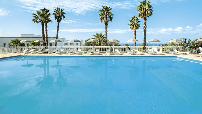 Grande piscina con lettini e ombrelloni, palme e cielo azzurro