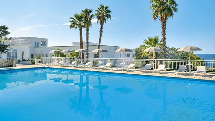 Piscina con lettini e ombrelloni, palme e vista sul mare