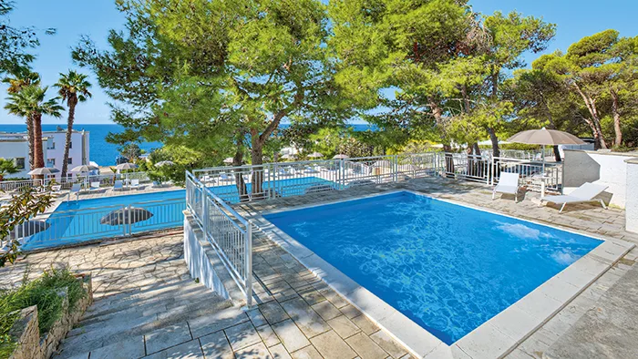 Piscina circondata da pini con vista sul mare e terrazza in pietra