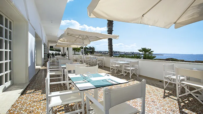 Terrazza ristorante all'aperto con tavoli bianchi, ombrelloni e vista mare
