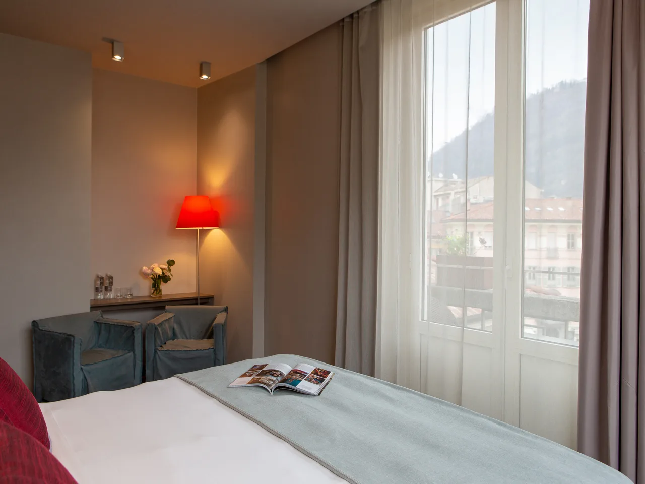 Camera con letto matrimoniale, poltrone blu, lampada rossa e vista sulle montagne dalla finestra
