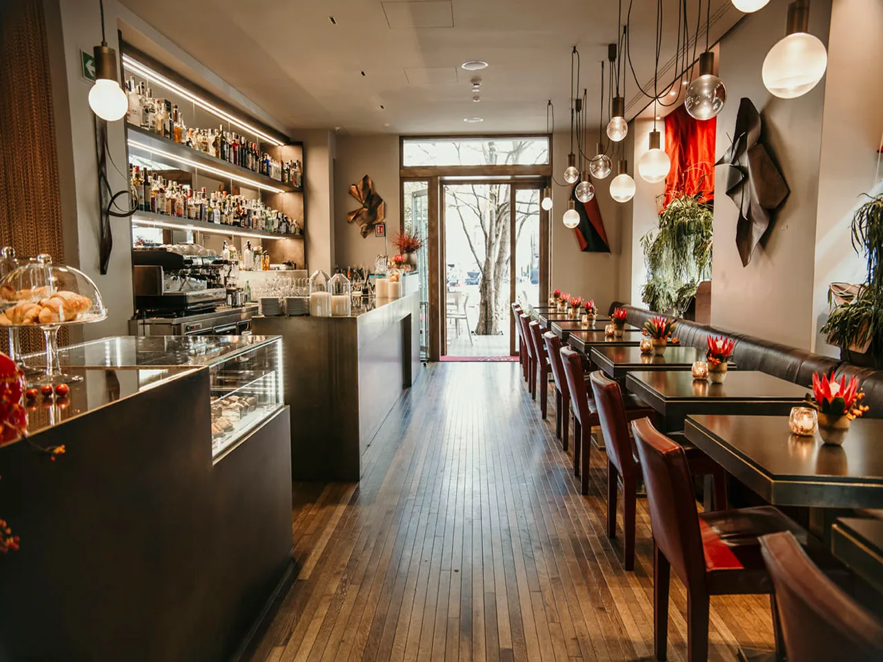 Bar del ristorante con lungo bancone, mensole di bottiglie illuminate e tavoli lungo la parete