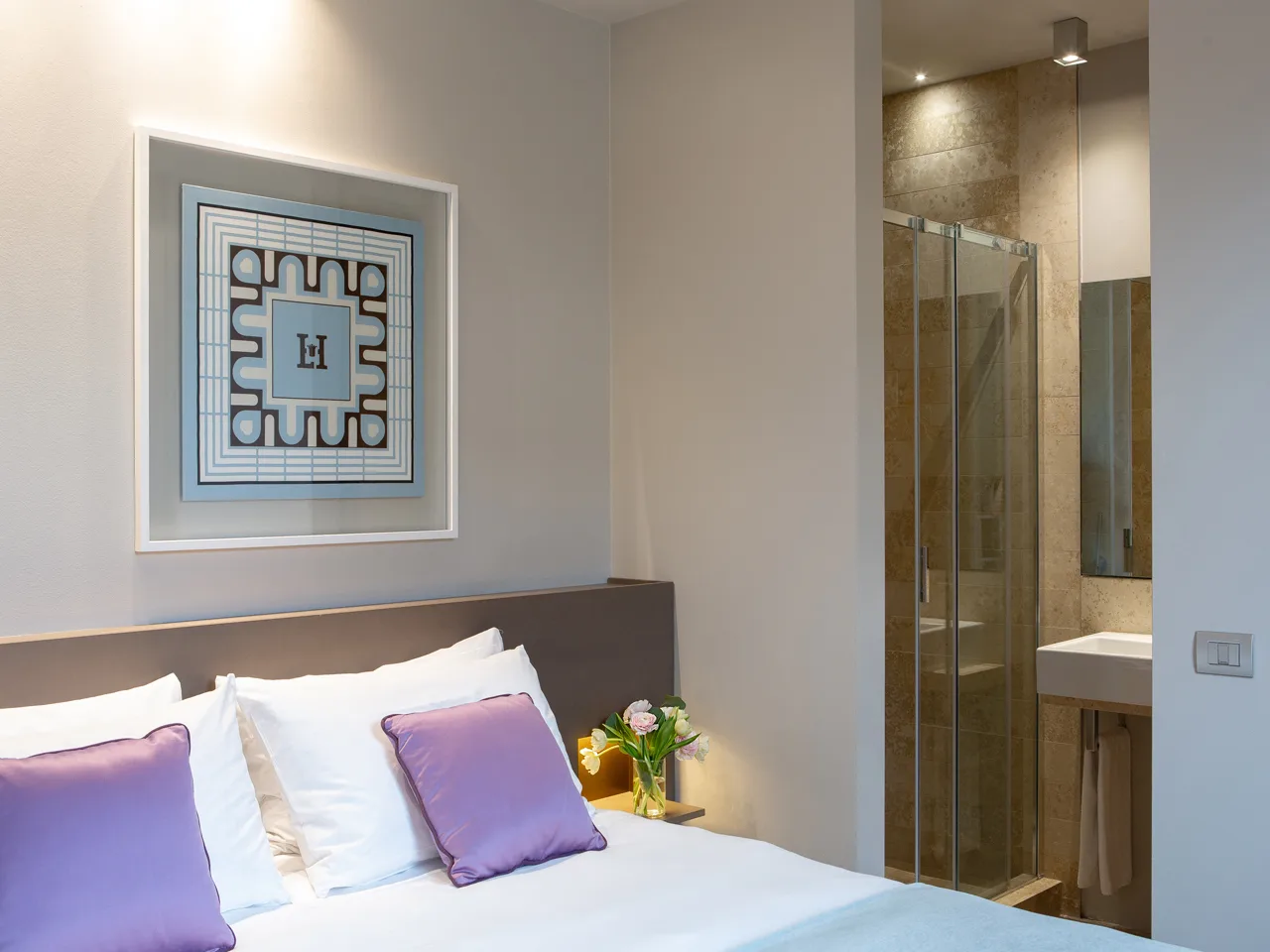 Camera matrimoniale con cuscini lilla, quadro decorativo e bagno con doccia in vetro annesso