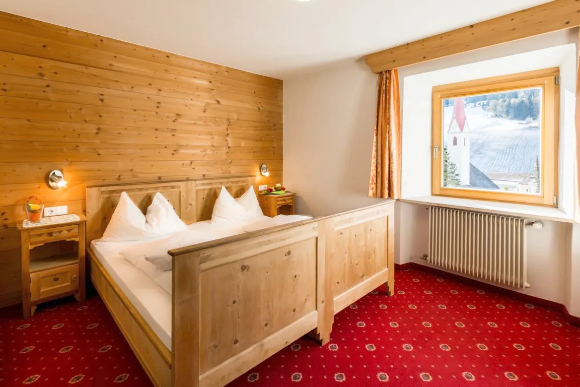 Camera da letto in stile alpino con parete in legno, moquette rossa e vista sul campanile