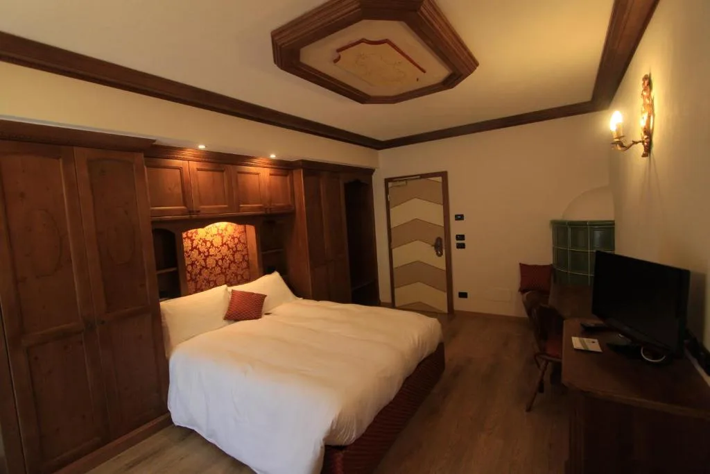 Camera matrimoniale con arredi in legno, letto e stufa in maiolica verde