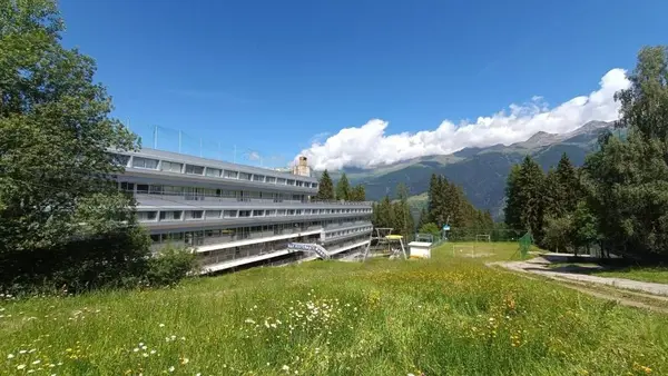 Edificio dell'hotel in montagna circondato da prato fiorito e vette alpine