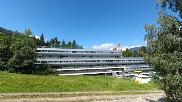 Facciata moderna della struttura immersa nel verde con montagne e cielo azzurro