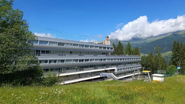 Struttura alberghiera con insegna Bar Ristorante circondata da prato e montagne