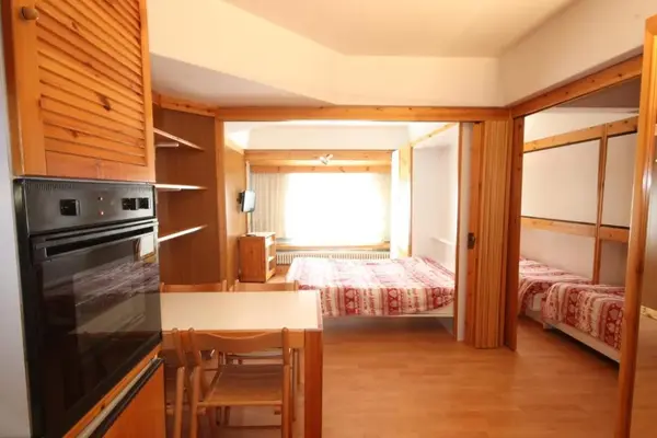 Interno di appartamento con cucina, forno, tavolo e camera da letto sullo sfondo