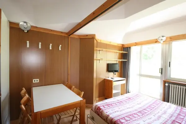 Camera con letto matrimoniale, tavolo, TV e balcone con vista sul verde