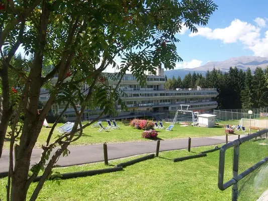 Vista estiva della struttura ricettiva tra alberi con prato, sdraio e montagne sullo sfondo