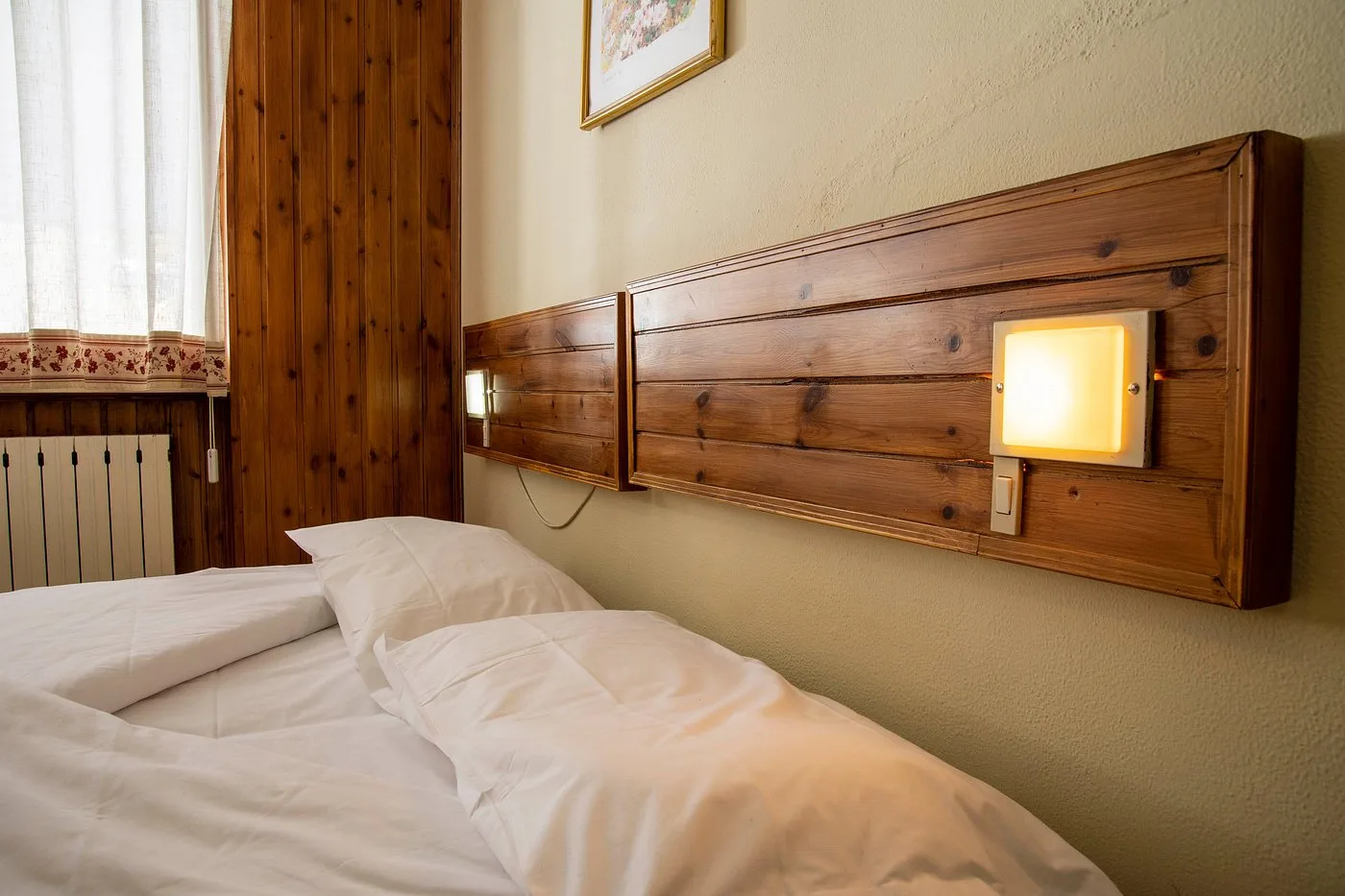 Testata del letto in legno con applique illuminata e finestra con tende bianche