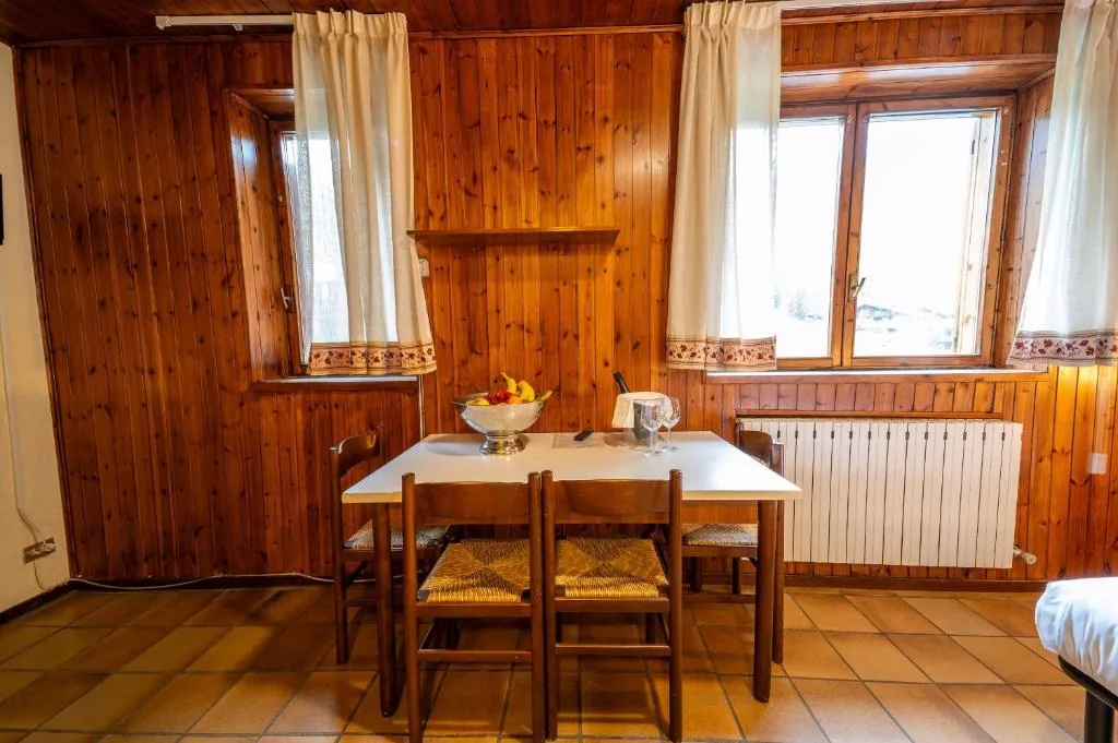 Angolo pranzo in legno con tavolo, sedie e finestre con tende bianche in camera rustica