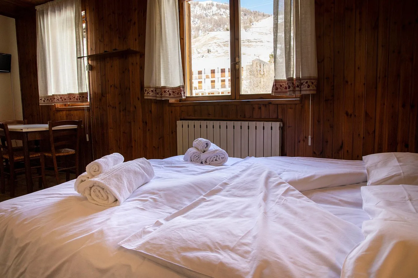 Letto matrimoniale con asciugamani arrotolati e vista sulle montagne innevate dalla finestra