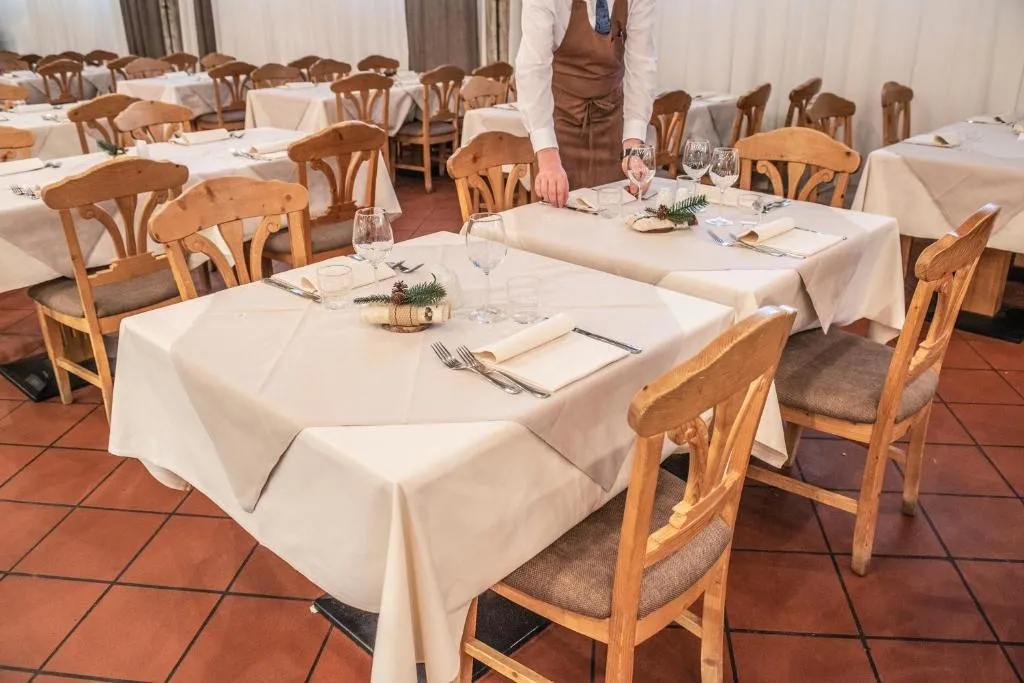 Sala ristorante con tavoli apparecchiati con tovaglie bianche e cameriere al lavoro