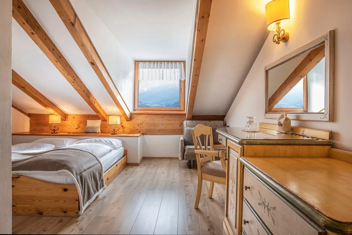 Camera mansardata con letto matrimoniale, travi in legno e finestra con vista sulle montagne