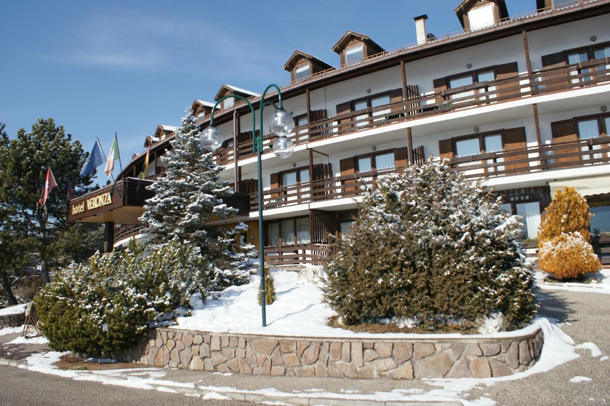 Facciata dell'hotel Veronza in inverno con neve, bandiere e giardino