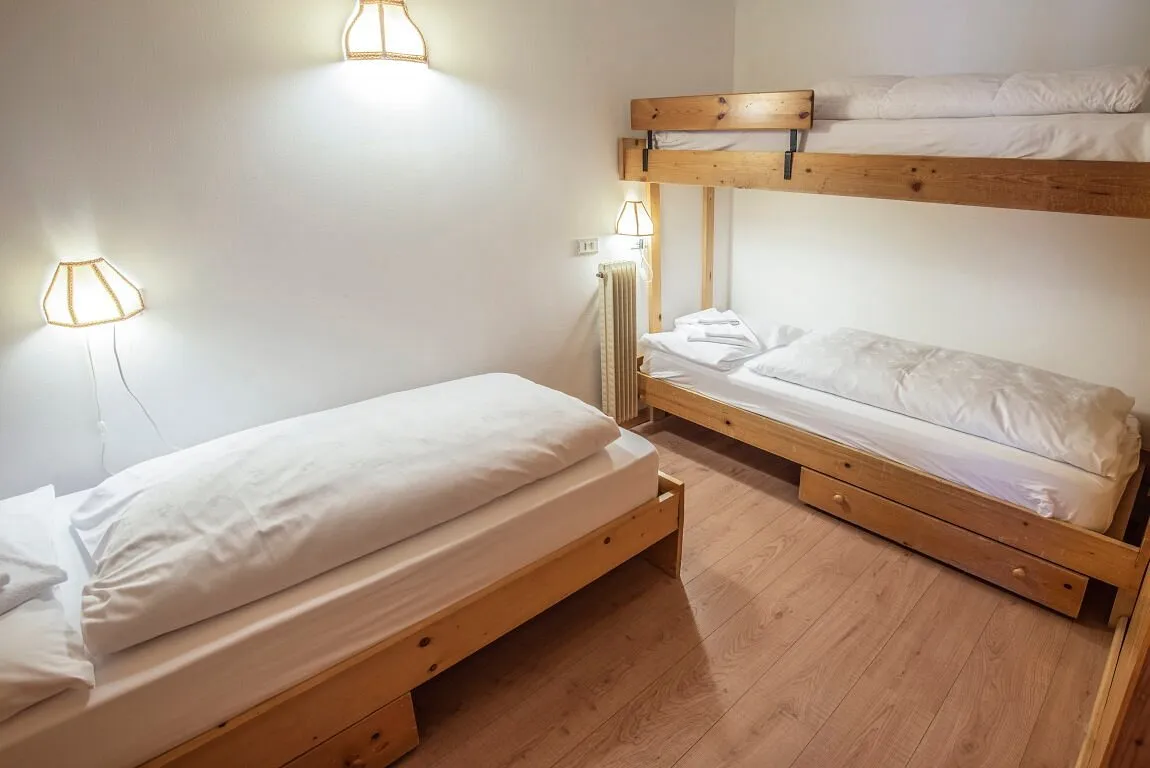 Camera con letto singolo e letto a castello in legno, lampade da parete e pavimento in legno