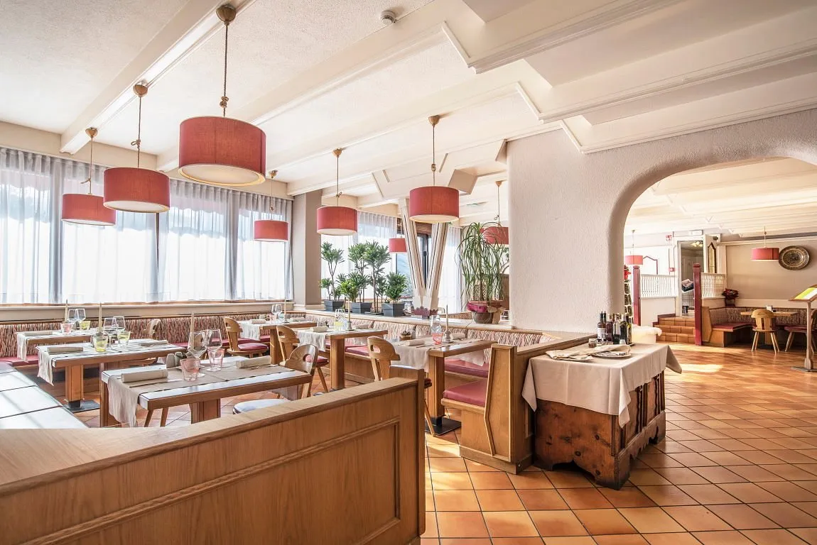 Sala ristorante con tavoli apparecchiati, panche imbottite e lampade a sospensione rosse