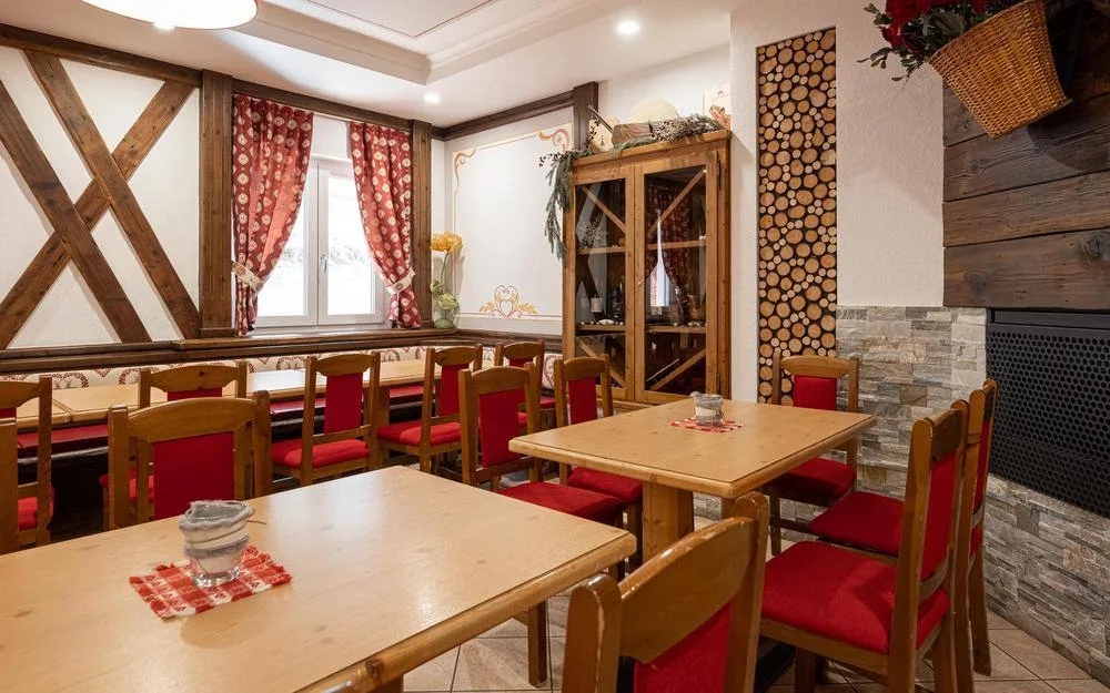 Angolo ristorante rustico con tavoli in legno, sedie rosse e travi a vista