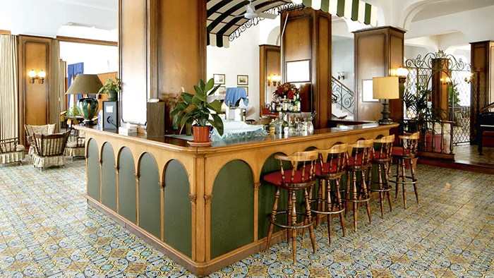 Bar interno dell'hotel con bancone in legno, sgabelli e pavimento a piastrelle decorate