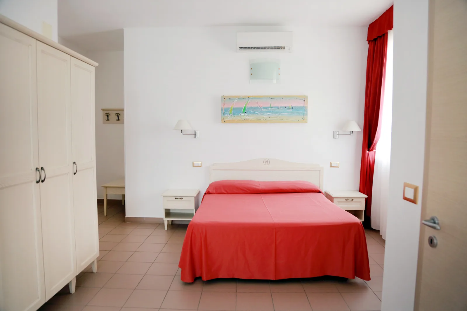 Camera matrimoniale con copriletto rosso, armadio bianco e aria condizionata