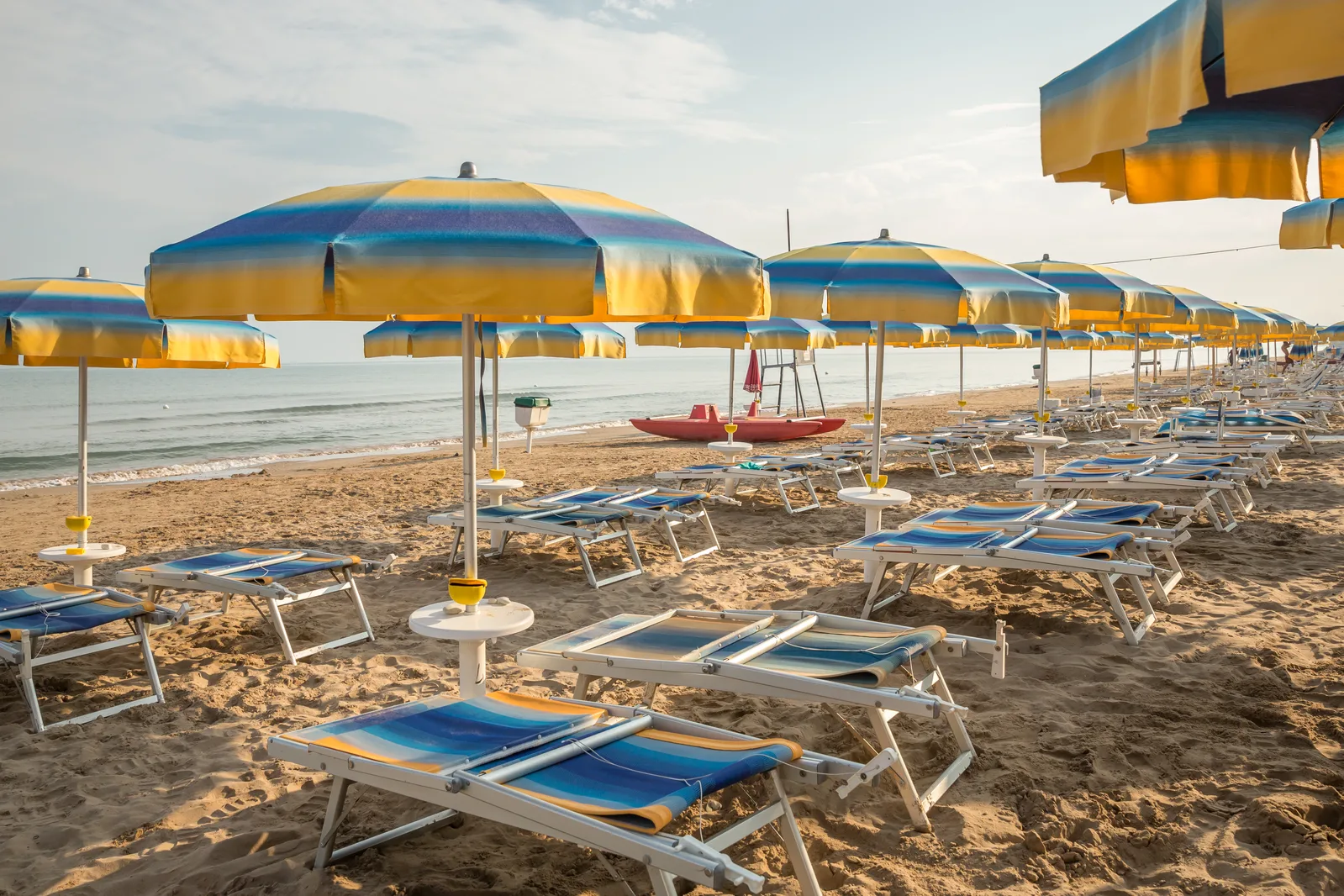 Spiaggia con ombrelloni gialli e blu, lettini e pedalò sul bagnasciuga