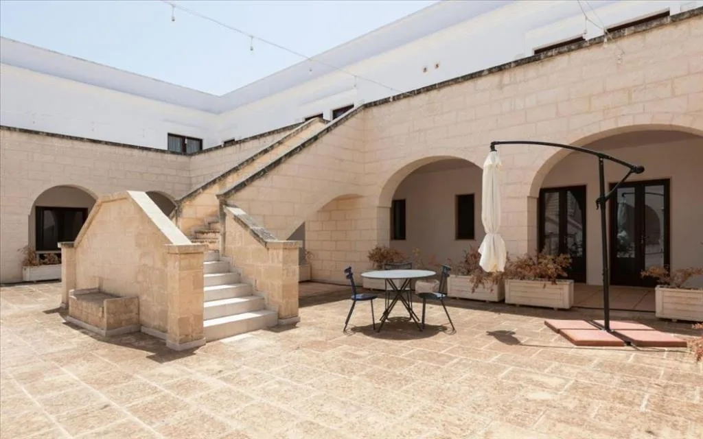 Cortile in pietra con scalinata esterna, arcate e area pranzo all'aperto