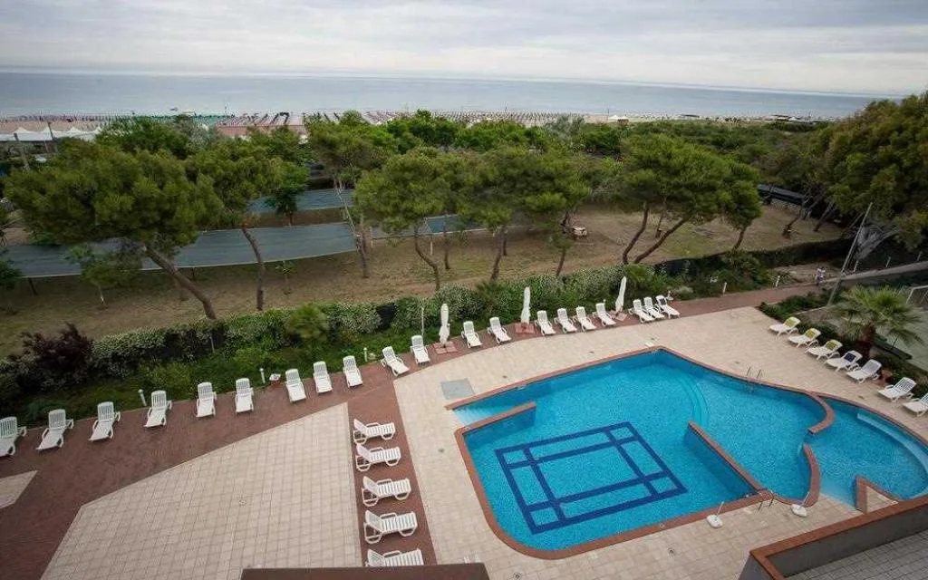 Vista panoramica su piscina, campo da tennis, pineta e mare sullo sfondo