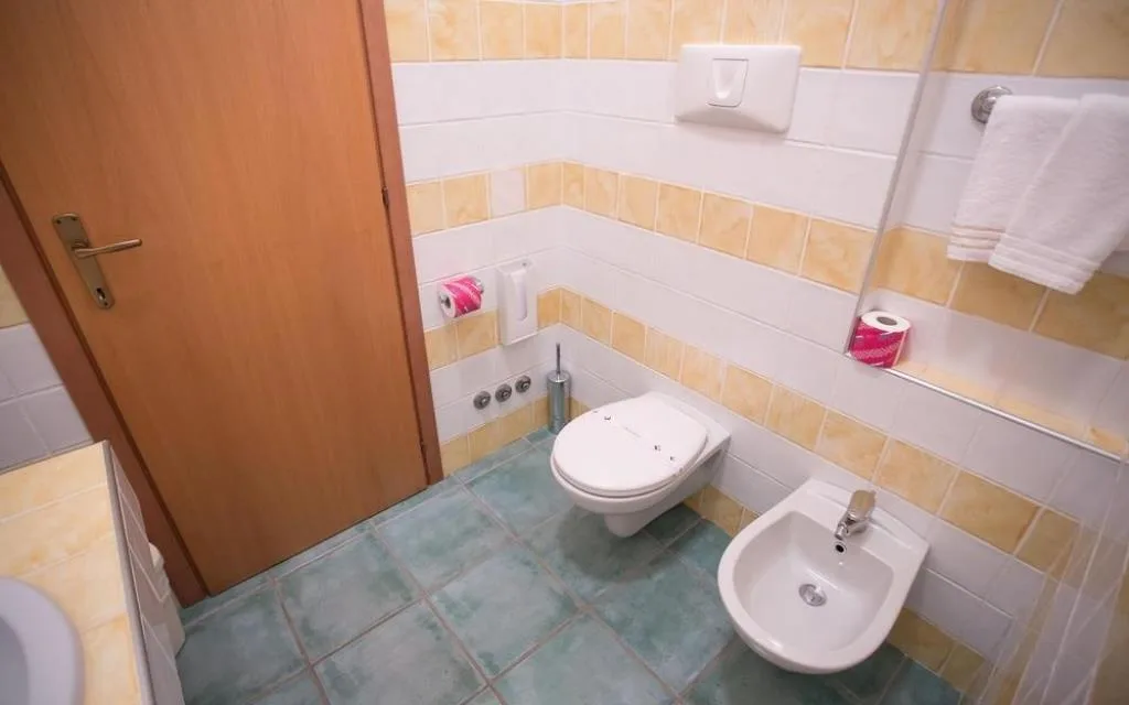 Bagno con piastrelle gialle e bianche, WC sospeso, bidet e porta in legno