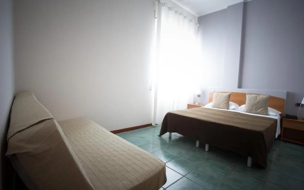 Camera tripla con letto matrimoniale e letto singolo, pavimento verde e finestra luminosa