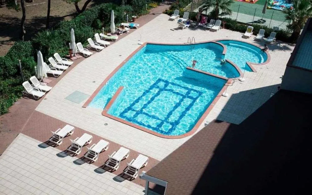 Vista dall'alto della piscina con lettini bianchi e pavimentazione in cotto circondata da vegetazione