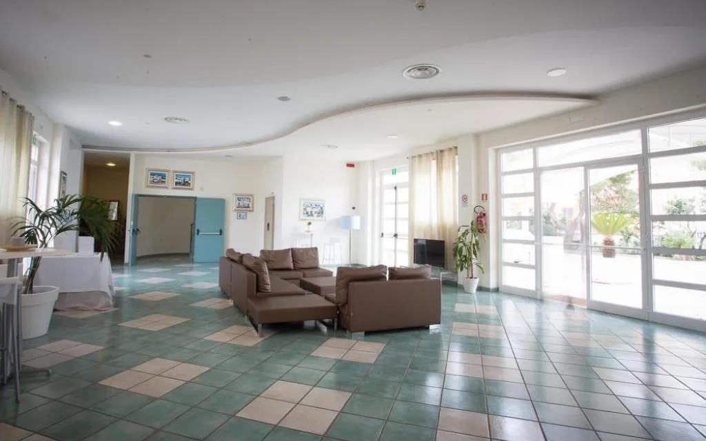Ampia hall dell'hotel con divani marroni, pavimento in mattonelle verdi e grandi vetrate