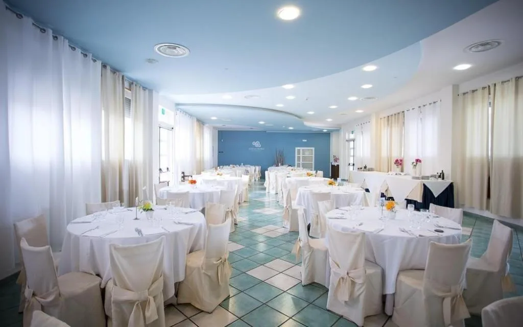 Sala da pranzo elegante con tavoli rotondi, tovaglie bianche e decorazioni floreali