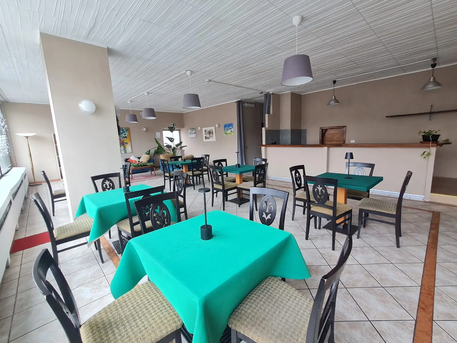 Sala da pranzo con tavoli vestiti di verde, sedie nere e ampie finestre